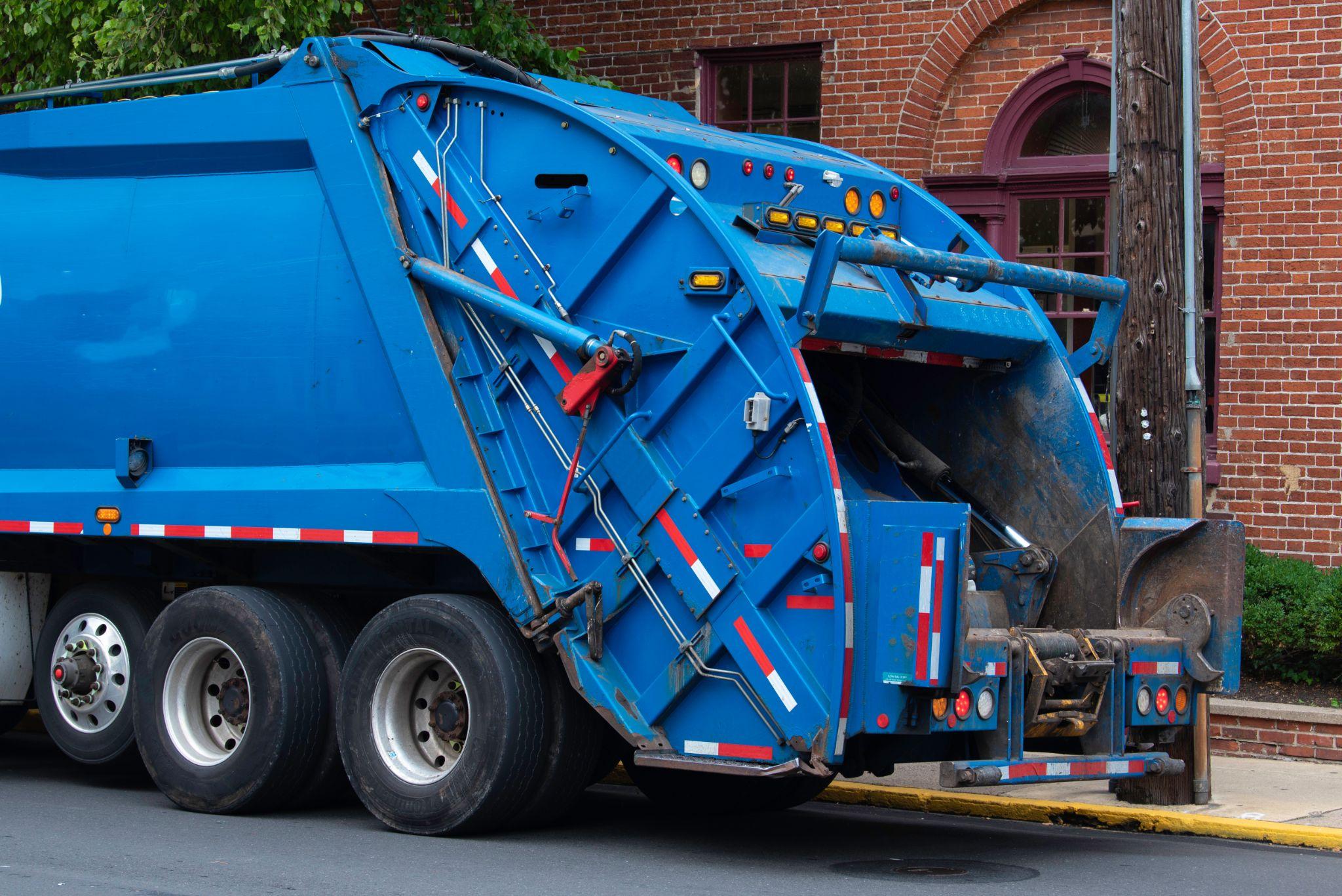 Blue garbage truck parked on street near brick building.