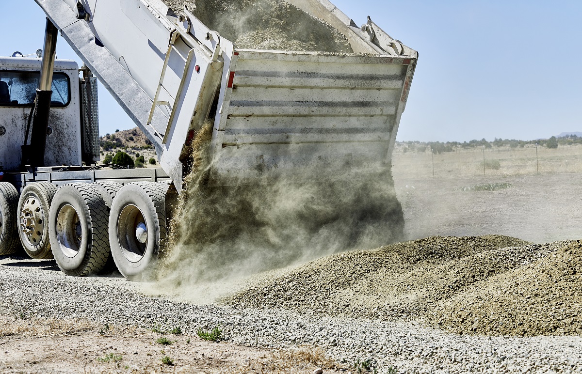 A dump truck spreading gravel on a dirt driveway