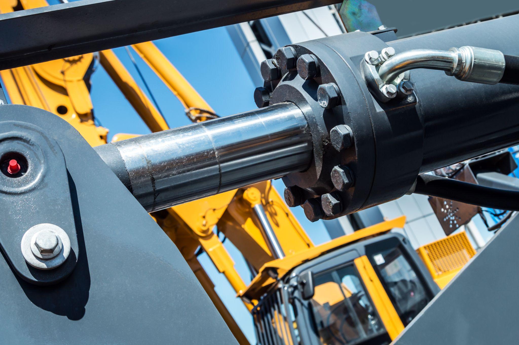 Hydraulic cylinder rod on construction equipment with machinery in background.