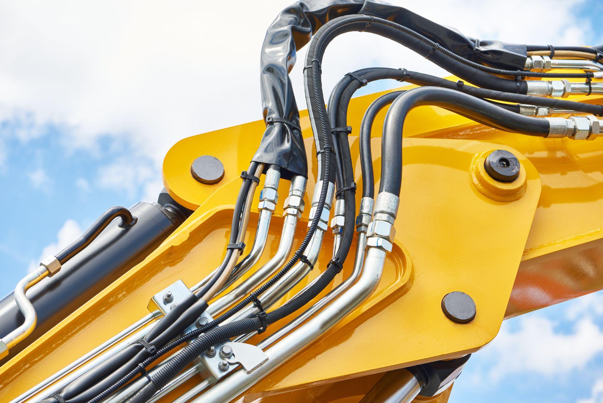 Hydraulic hoses and fittings on yellow construction machinery arm.