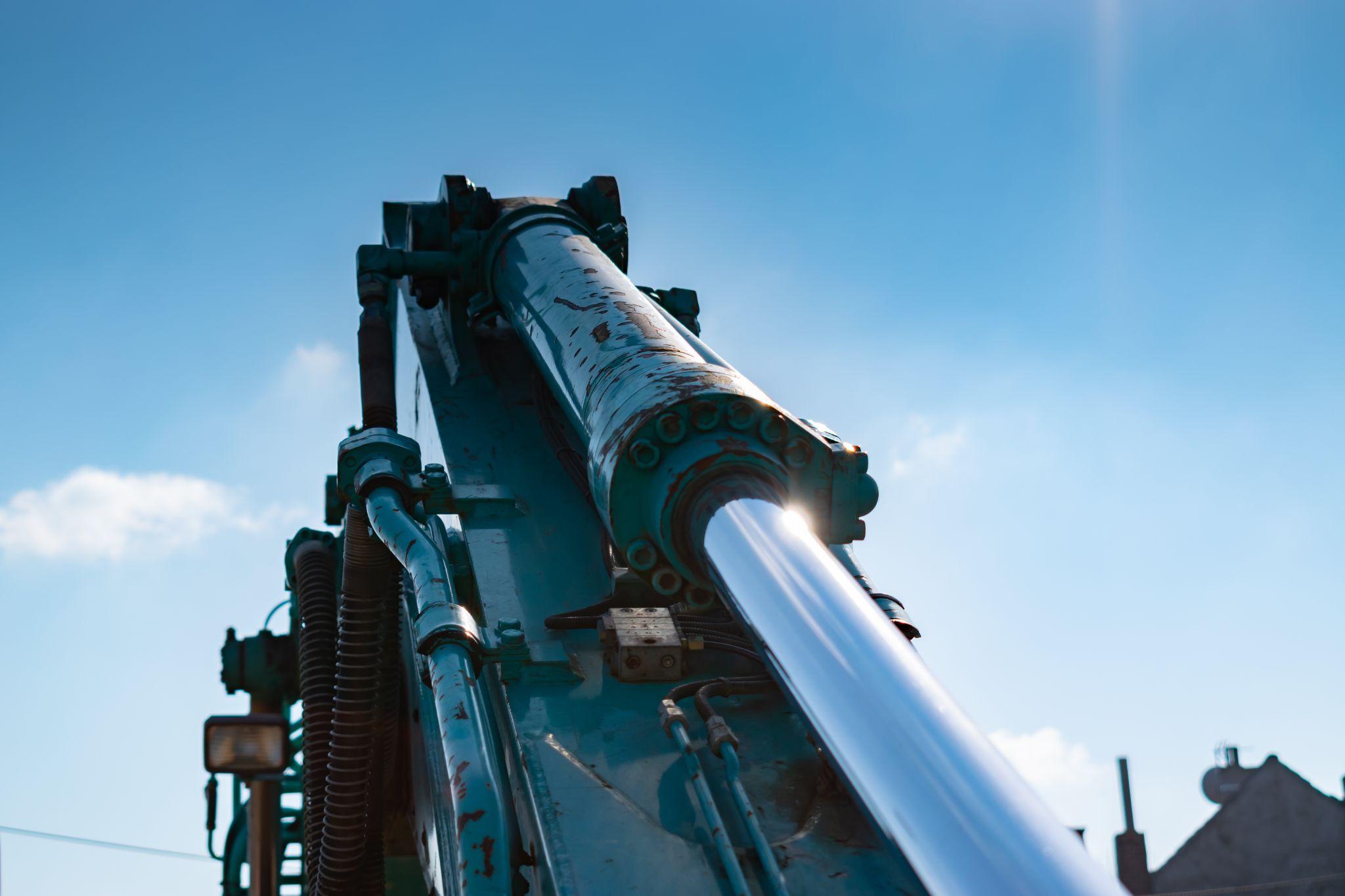 Extended hydraulic cylinder rod on heavy construction machinery under blue sky.