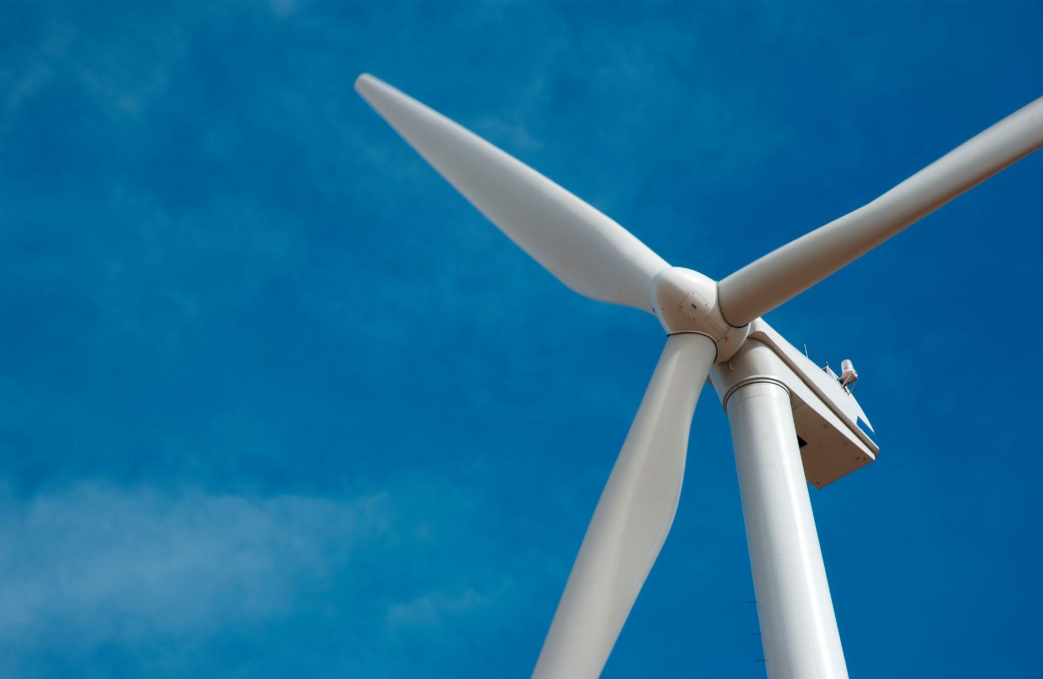 Large wind turbine with rotating blades against a clear blue sky.